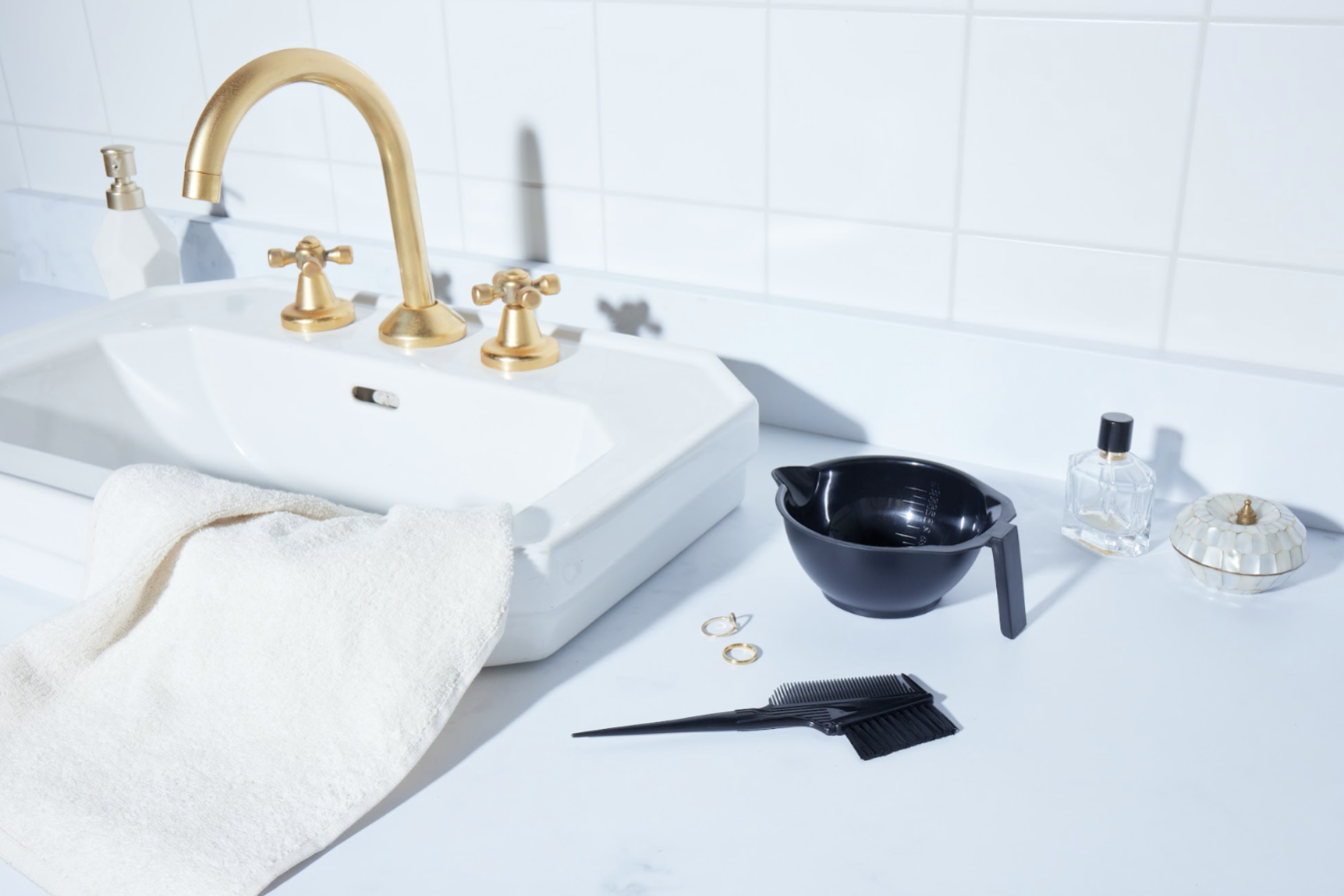 Ein weißes Waschbecken mit einem weiß gefliesten Hintergrund und einem Kamm und einer Haarfärbeschale, die für die Clairol Color Studio Reihe bereitstehen.